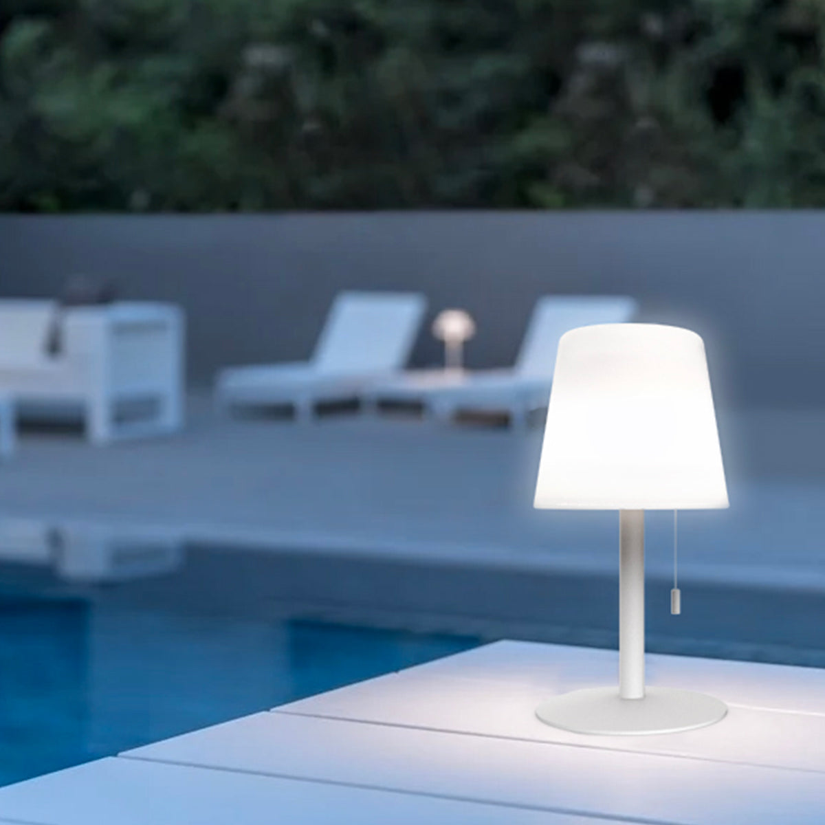 Qushini Bold Lamp bianca accesa all'aperto, sul bordo di una piscina